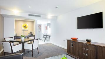 A modern hotel room with a dining area, a flat-screen TV, and a wooden cabinet.