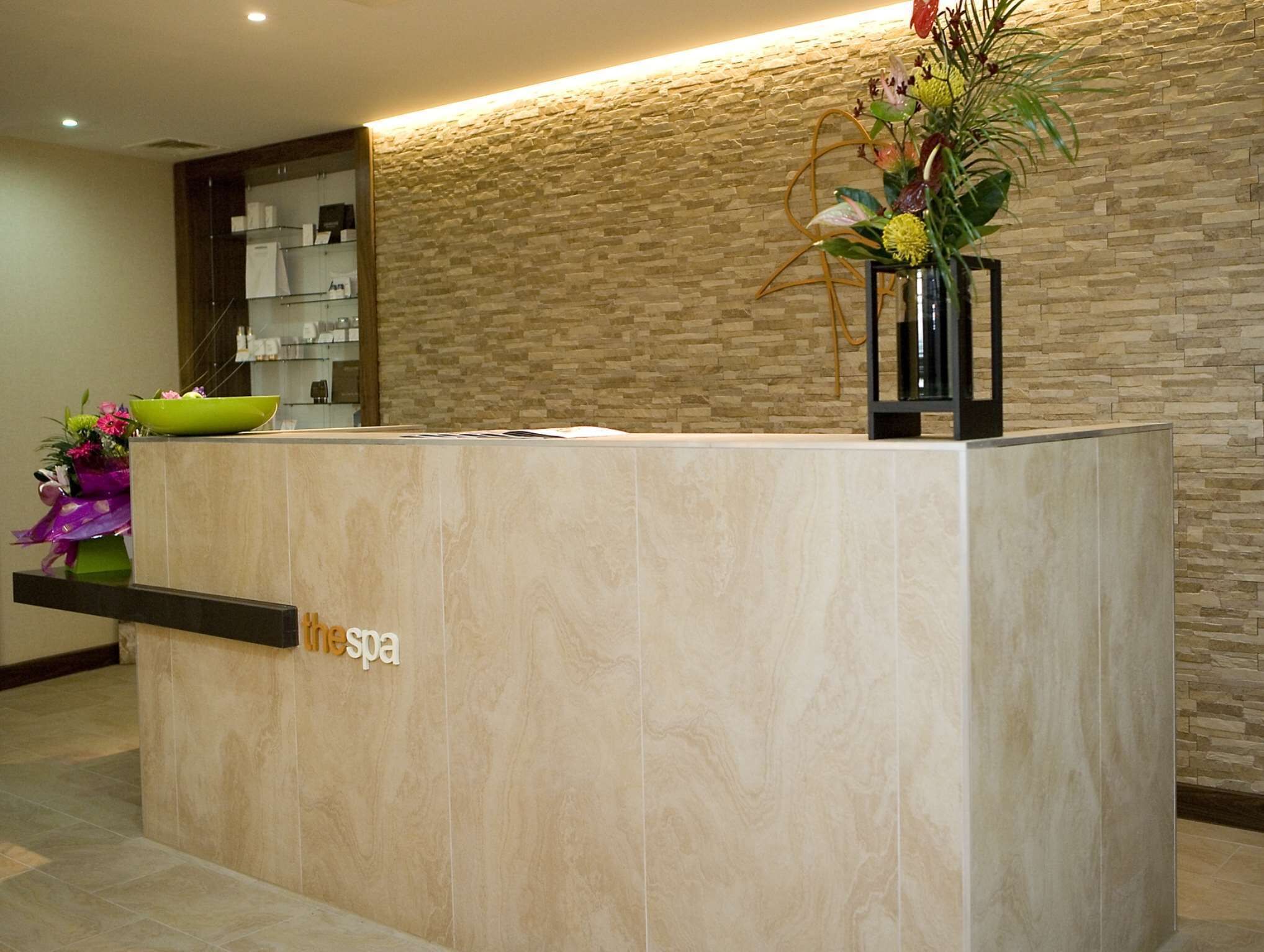 A reception desk with a stone wall background, a green bowl, and a vase with flowers.