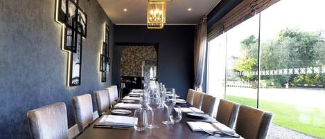 A long dining table with chairs, framed pictures on the wall, and a view of the outdoors.