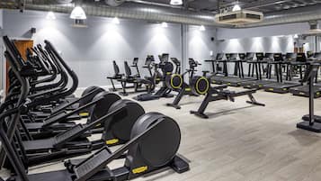 A gym with multiple treadmills, elliptical machines, and stationary bikes arranged in rows.