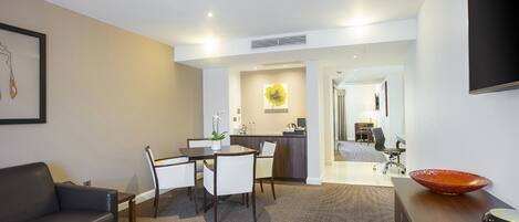 A modern living room with a sofa, coffee table, and dining area. There is a kitchen in the background with a large flower on the wall.