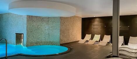 A modern spa area with a circular hot tub, reclining chairs, and a textured wall.