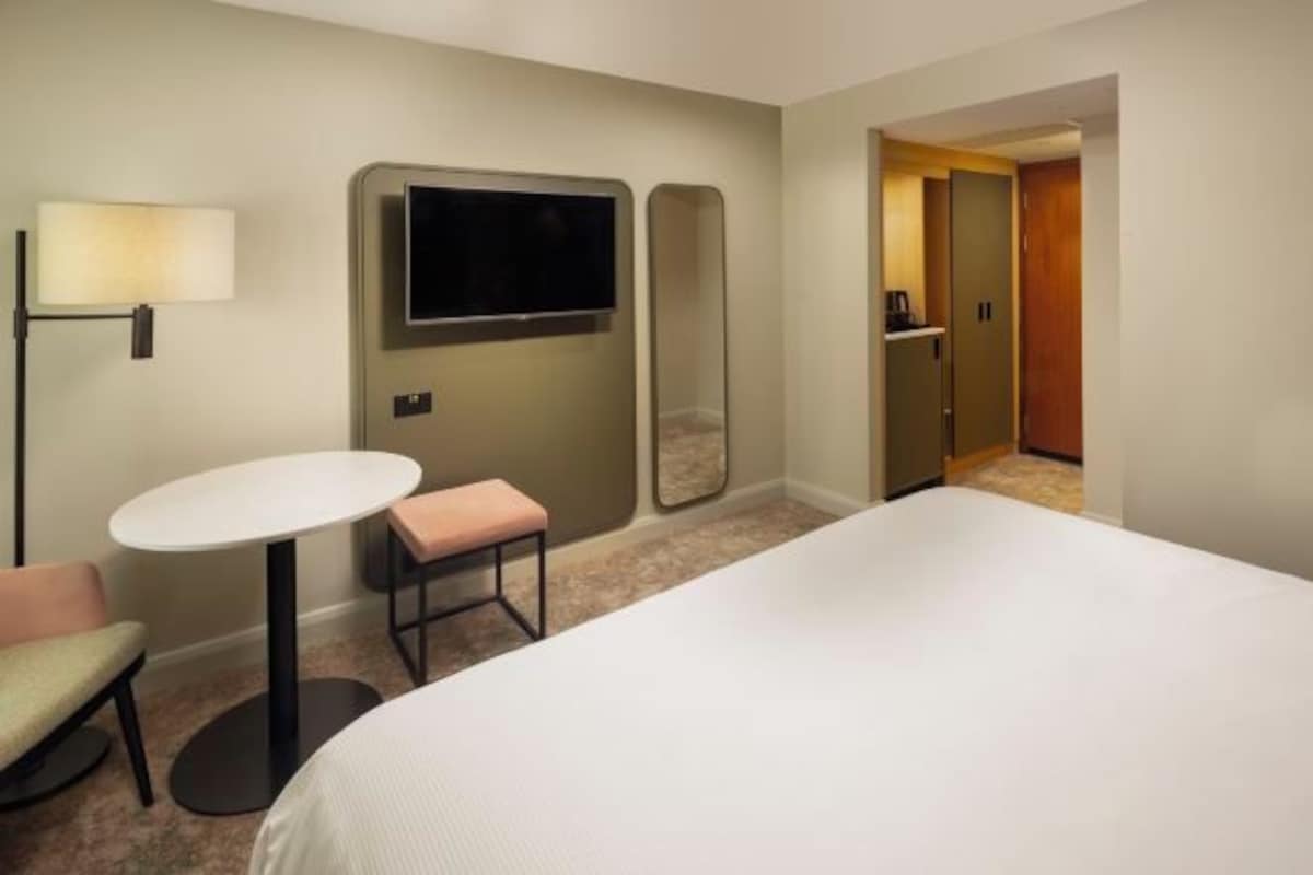 Une chambre d’hôtel avec un lit, une petite table ronde et un banc, un téléviseur fixé au mur et un miroir.
