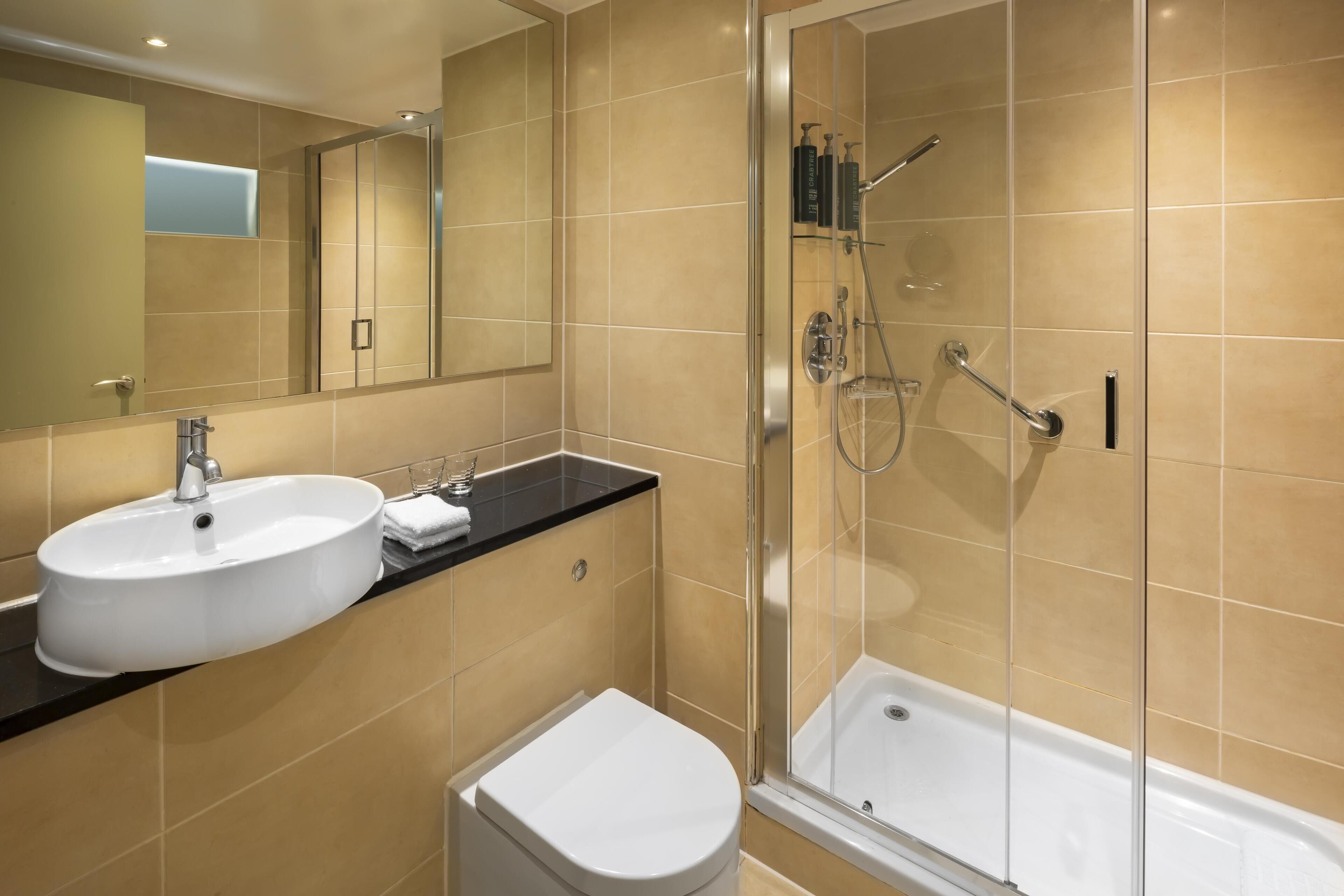 A modern bathroom with a white sink, a toilet, and a glass-enclosed shower area.