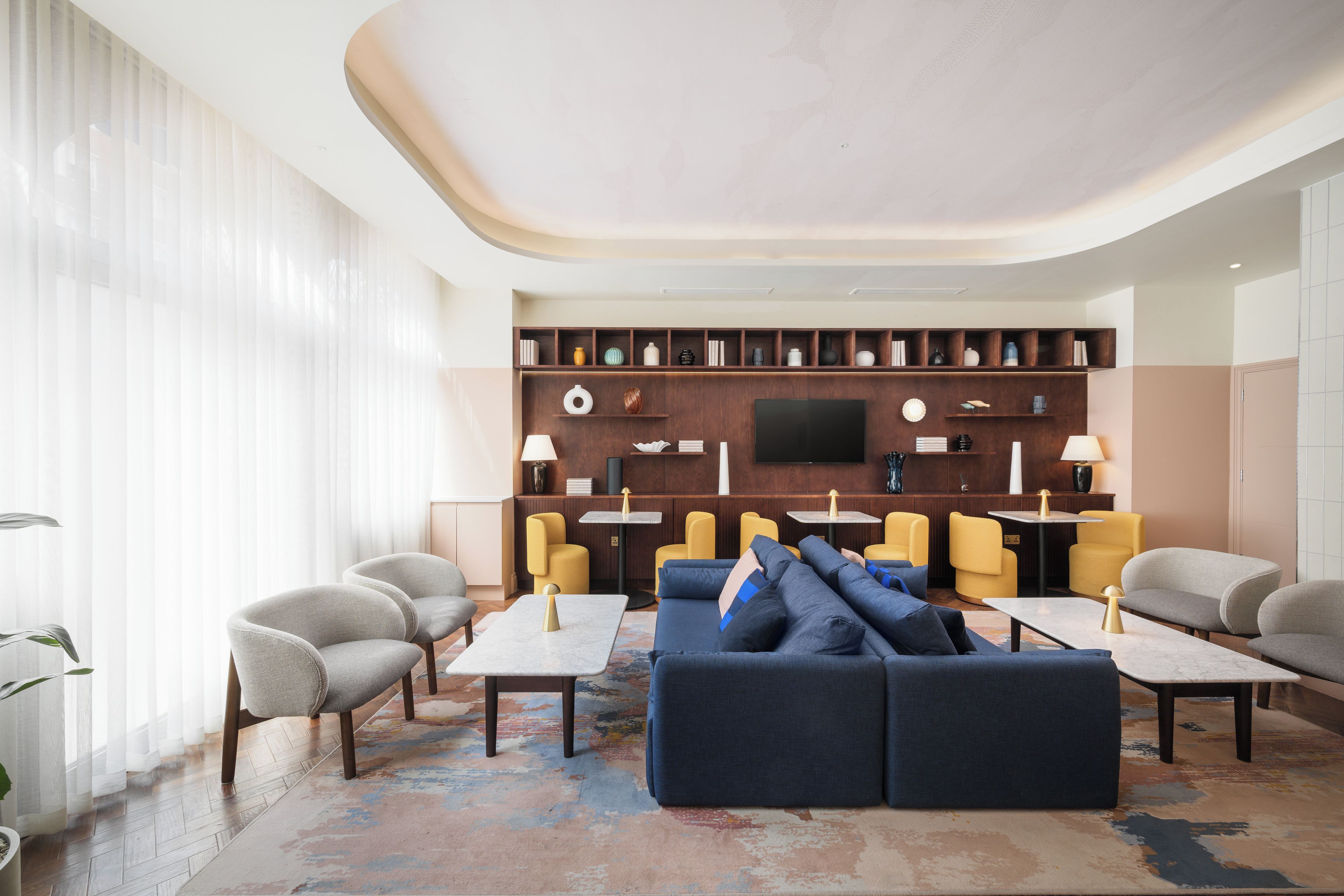 A modern living room with a sectional sofa, armchairs, a flat-screen TV, and a bookshelf.