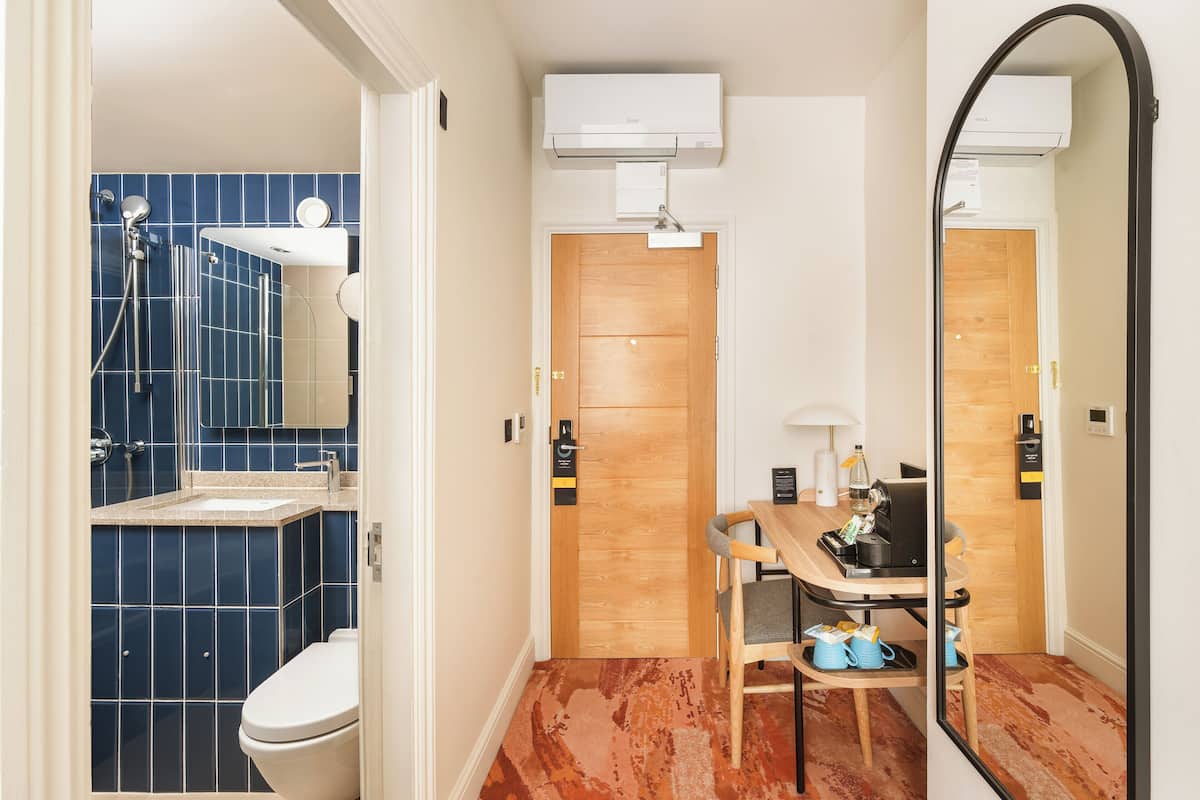 Ein Badezimmer mit einer blauen Duschkabine, einer weißen Toilette, einer Holztür und einem Spiegel, der den Raum widerspiegelt.