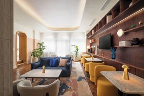 A modern lounge area with a sofa, armchairs, a coffee table, and a television on a wooden wall. - voco London – Bloomsbury by IHG (London)
