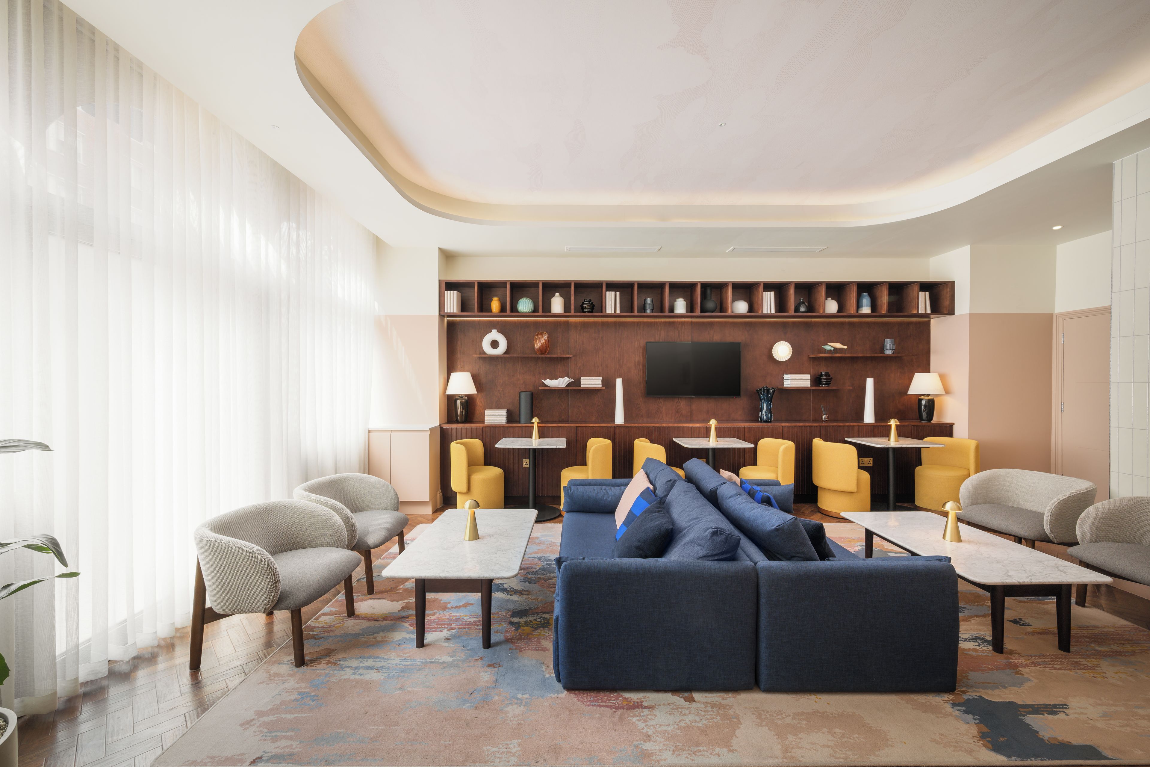 A modern living room with a sectional sofa, armchairs, a coffee table, and a flat-screen TV mounted on a wooden wall.