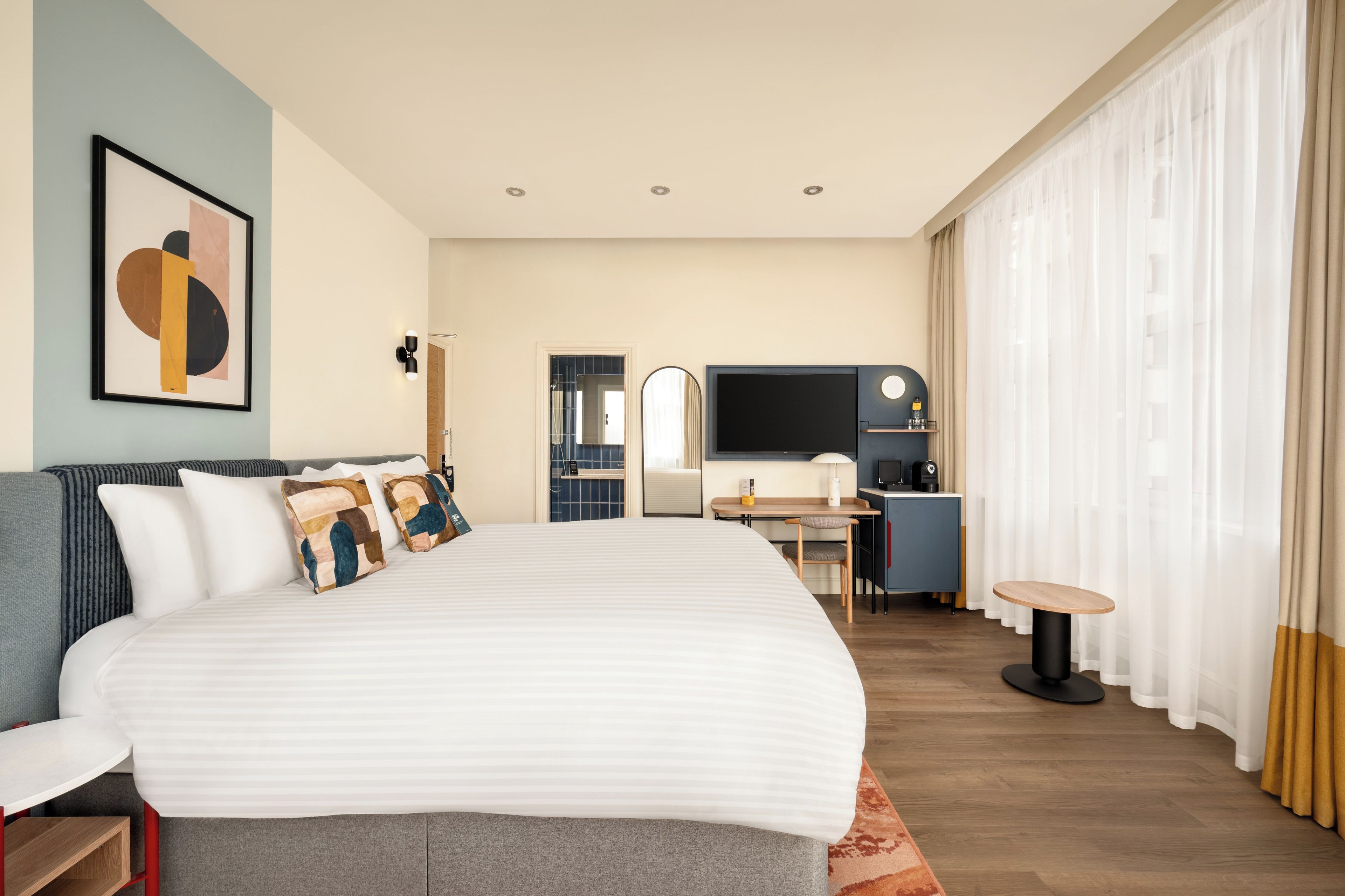 Een hotelkamer met een groot bed, een bureau, een televisie en een badkamer zichtbaar door een open deur.