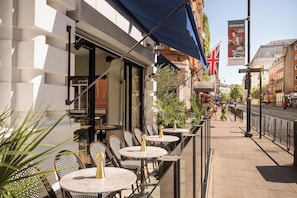 An outdoor seating area with tables and chairs, a blue awning, and a British flag. - voco London – Bloomsbury by IHG (London)