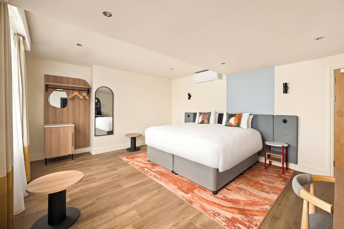 Ein modernes Hotelzimmer mit einem großen Bett, einem runden Tisch, einem Kleiderschrank und einem Spiegel.