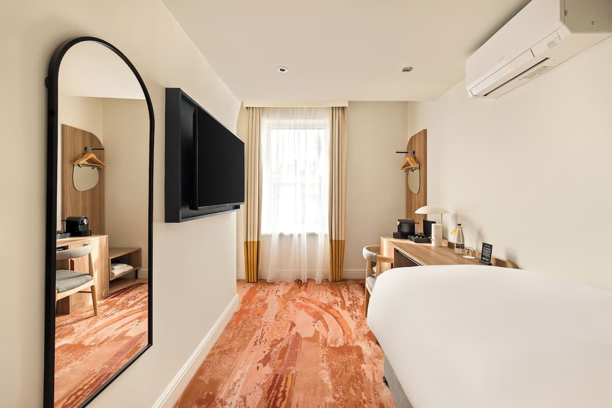 Ein Hotelzimmer mit Bett, Schreibtisch, Stuhl, Fernseher, Spiegel und Klimaanlage.
