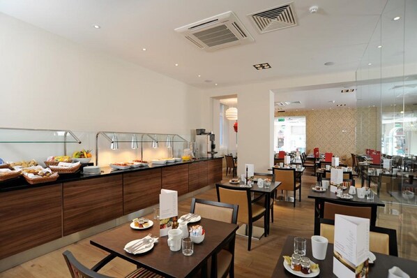 A modern hotel dining area with a buffet setup, multiple dining tables, and a glass partition separating the buffet from the seating area.