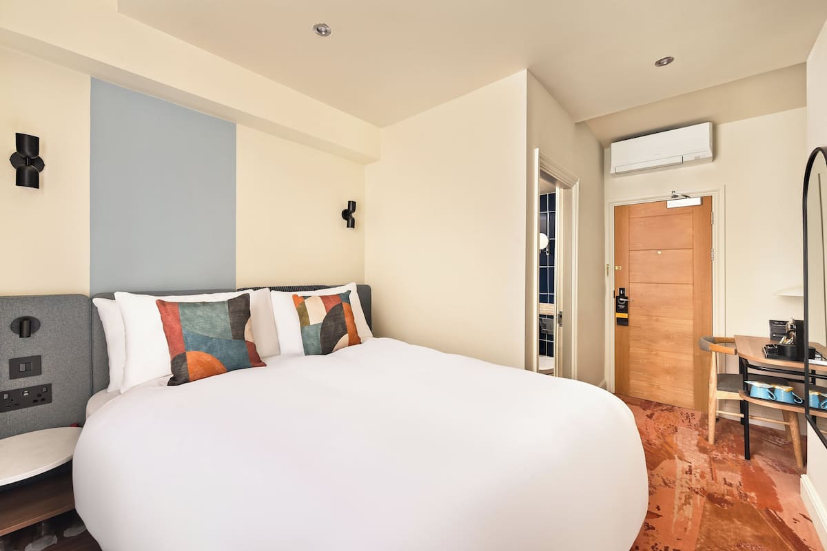 Ein Hotelzimmer mit einem großen Bett, einem Schreibtisch mit Stuhl, einem Kleiderschrank und einer Klimaanlage.