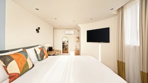 Ein Hotelzimmer mit einem großen Bett, einem an der Wand montierten Flachbildfernseher, einem Schreibtisch mit Stuhl und einem Fenster mit Vorhängen.