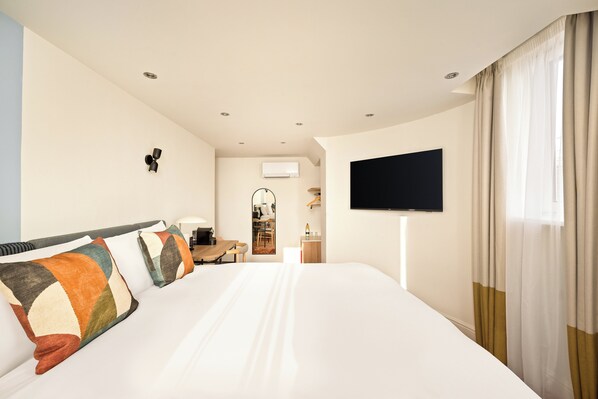 Una habitación de hotel con una cama grande, un televisor de pantalla plana montado en la pared, un escritorio con una silla y una ventana con cortinas.