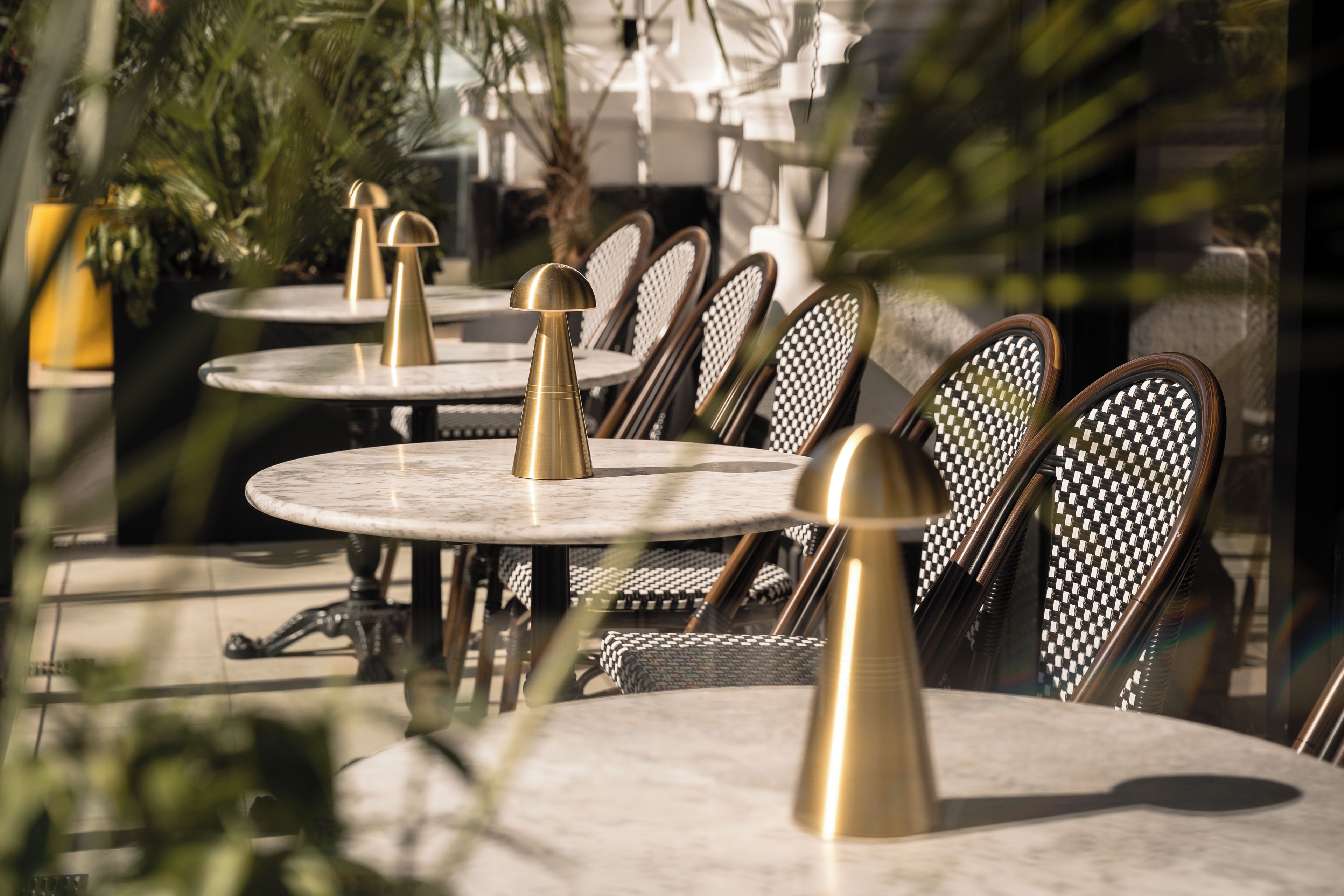 Buiten gelegen ronde tafels met metalen stoelen en een centraal hanglamp.