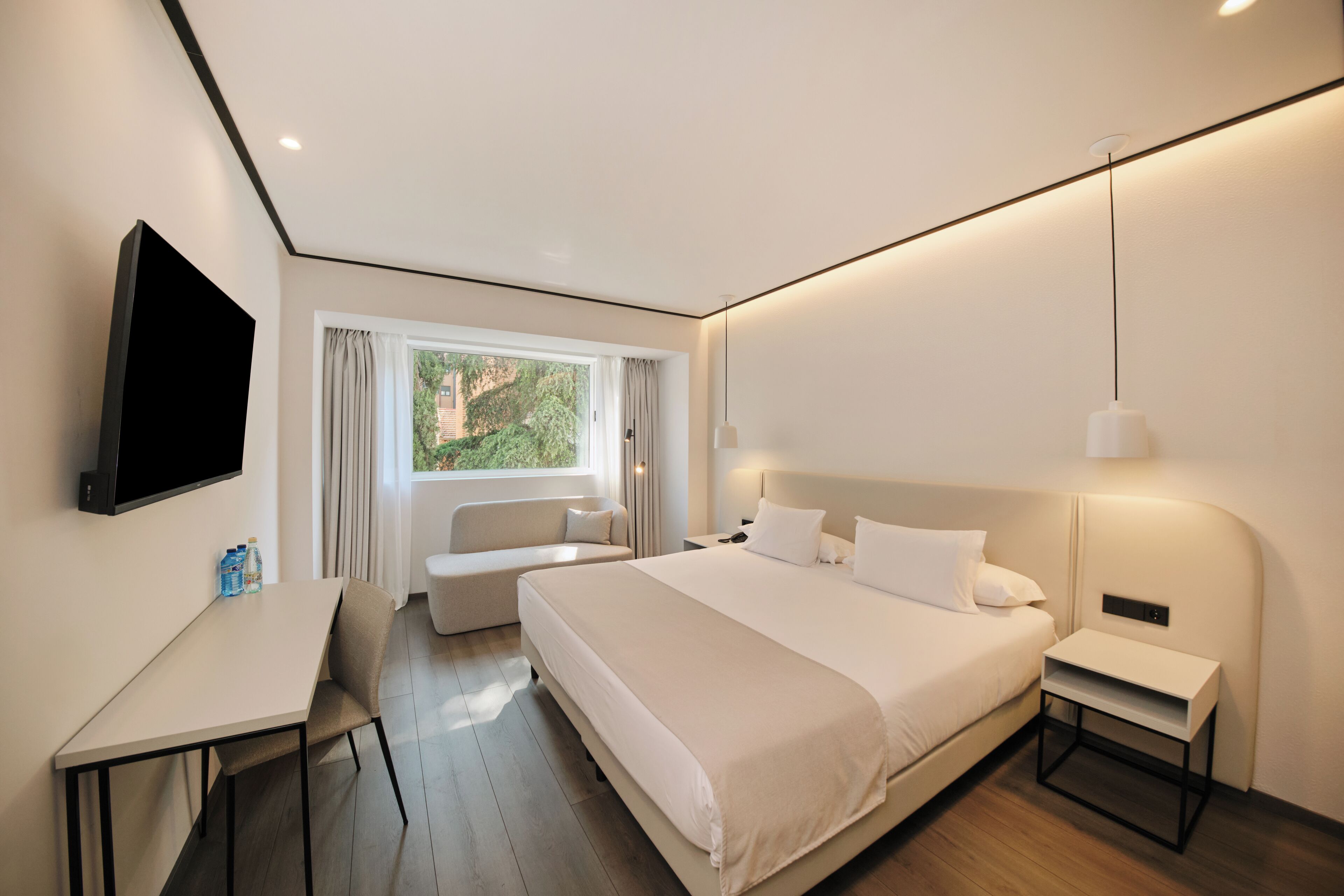 Una habitación de hotel moderna con una cama grande, un escritorio, un sofá y un televisor.