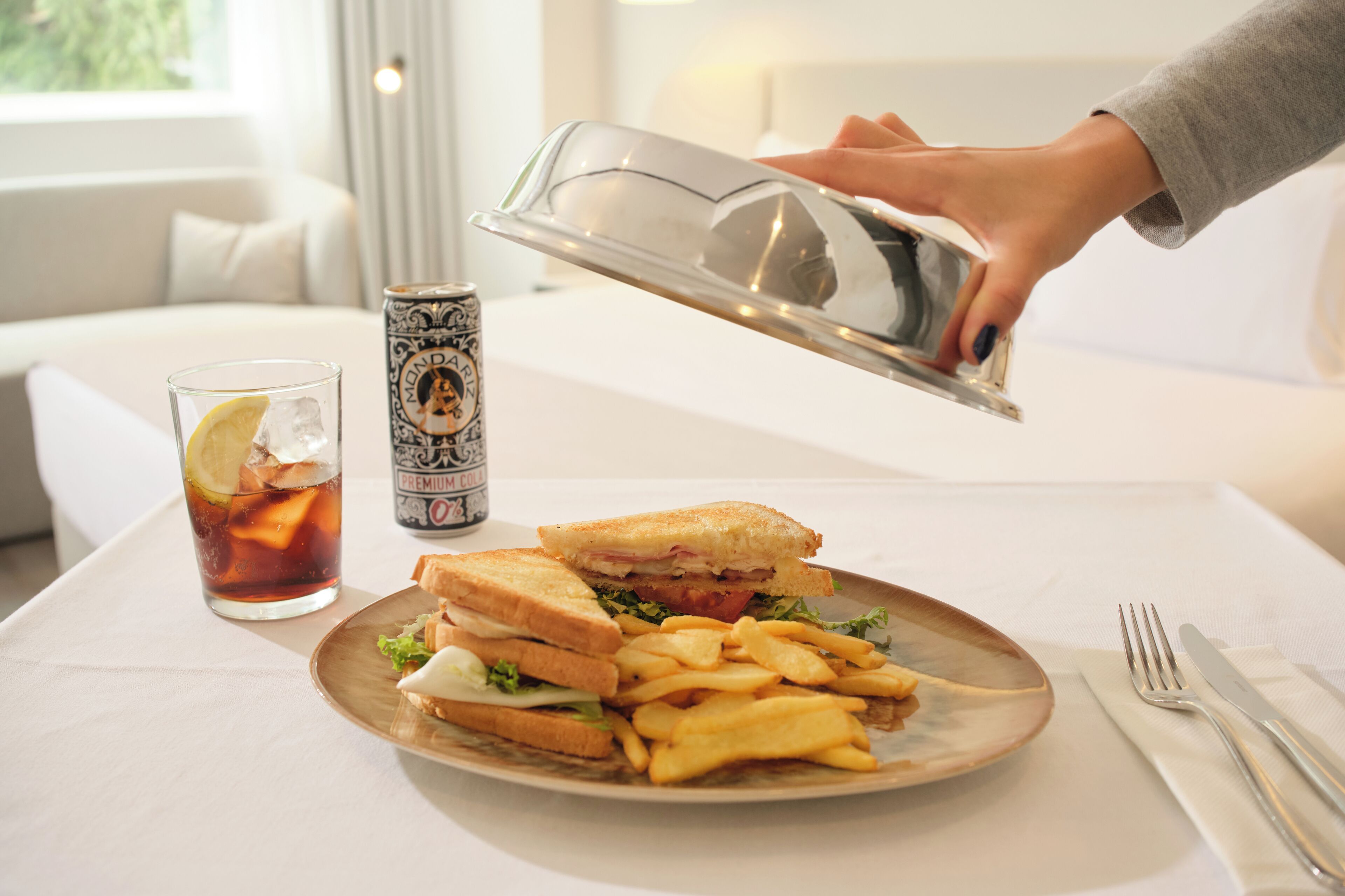 Une assiette avec un sandwich et des frites, un verre de thé glacé et une canette de soda sur une table.