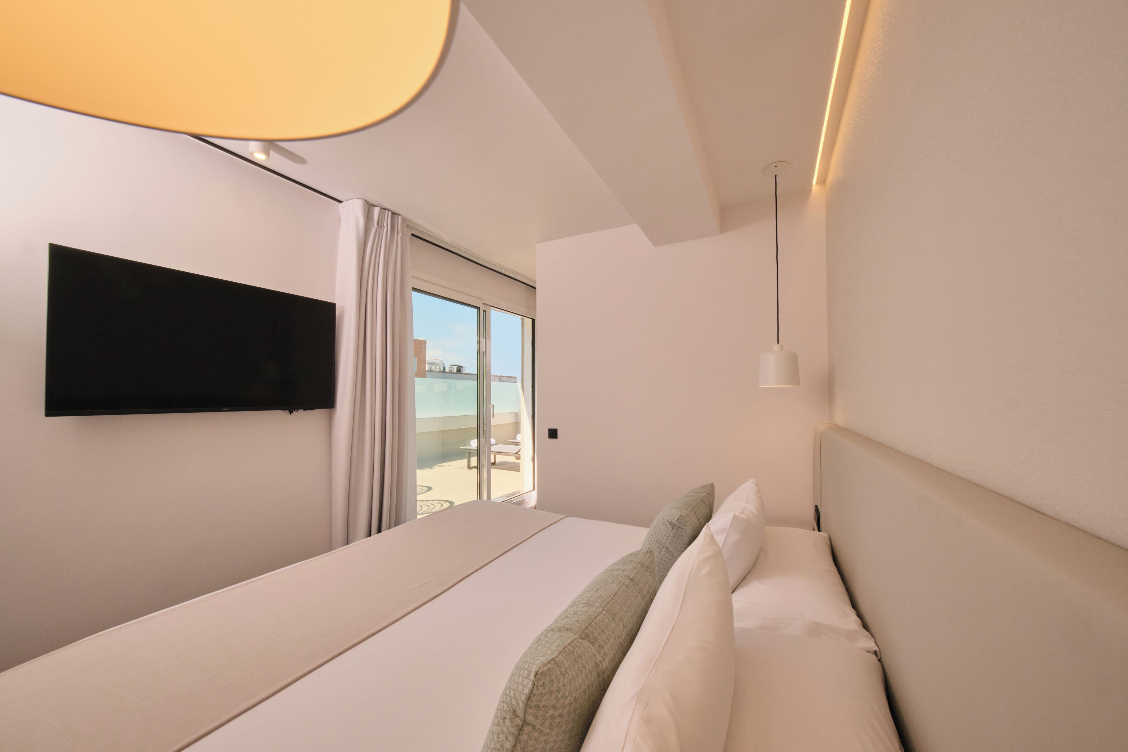 Une chambre d’hôtel moderne dotée d’un grand lit, d’un téléviseur à écran plat fixé au mur et offrant une vue sur l’extérieur grâce à une porte-fenêtre coulissante.