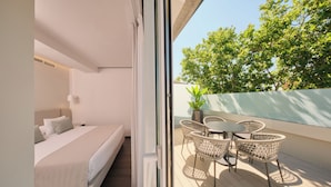 A modern bedroom with a bed, bedside table, and a view of a balcony with wicker chairs and a potted plant. - 1881 Madrid Ventas Hotel (Madrid)