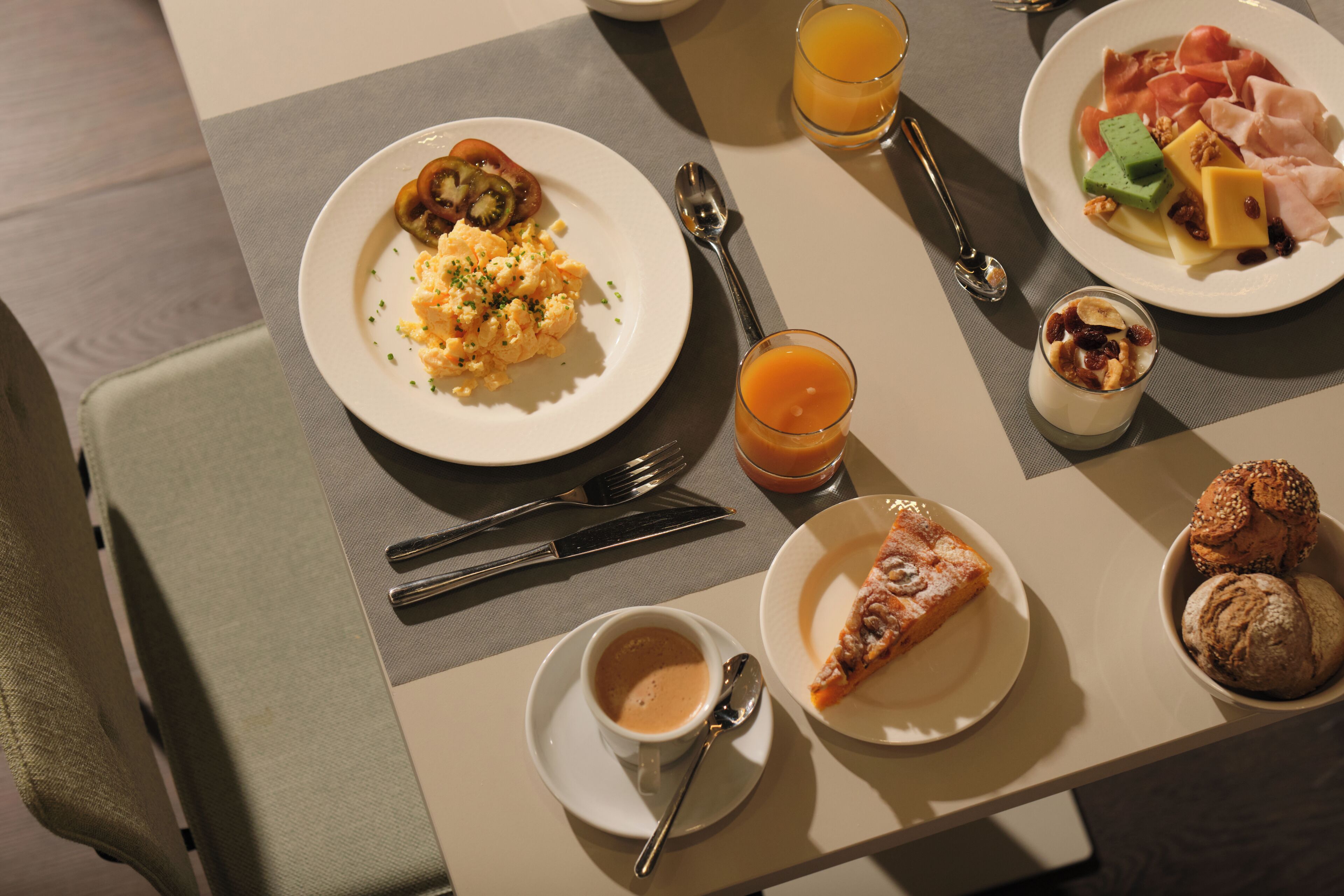 Desayuno con huevos revueltos, tostadas, una porción de pizza, un tazón de sopa y un vaso de jugo de naranja.