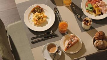 Desayuno con huevos revueltos, tostadas, una porción de pizza, un tazón de sopa y un vaso de jugo de naranja.