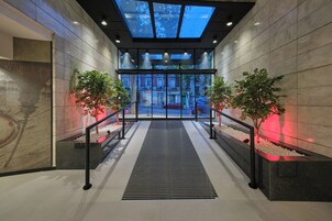 A modern indoor entrance with a glass ceiling, a central staircase, and potted plants.
