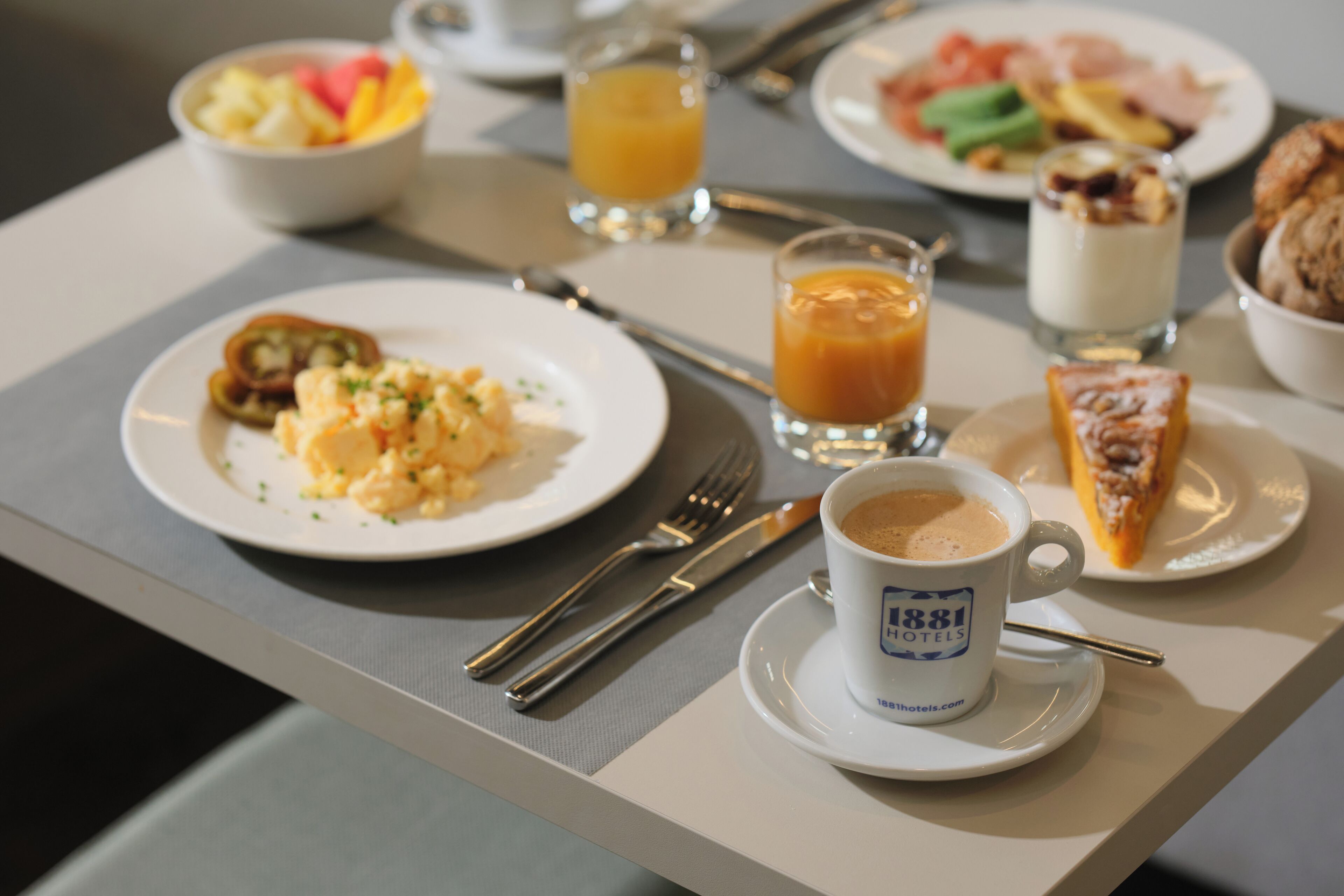 Una mesa de desayuno con platos de comida, una taza de café y un vaso de jugo de naranja.