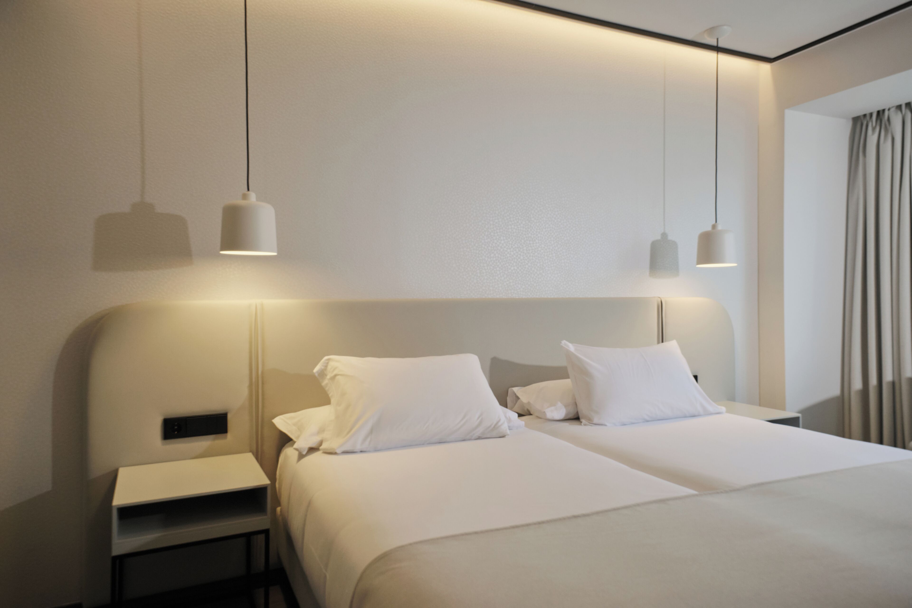Habitación de hotel moderna con dos camas, una mesita de noche e iluminación colgante.