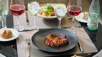 Una mesa de comedor con un plato de pulpo, copas de vino, una botella de agua Vichy Catalan y un muffin.