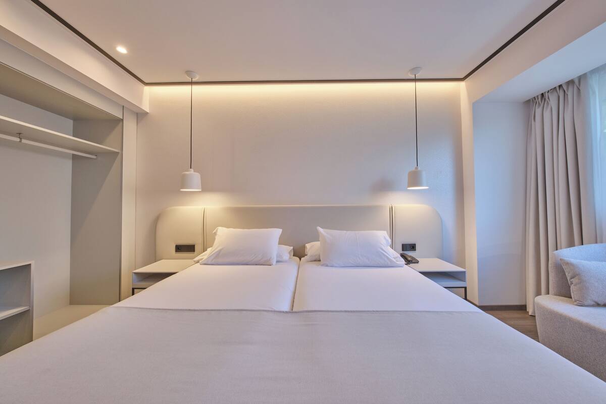 A modern hotel room with a large bed, bedside tables, a wardrobe, and a view of the city.