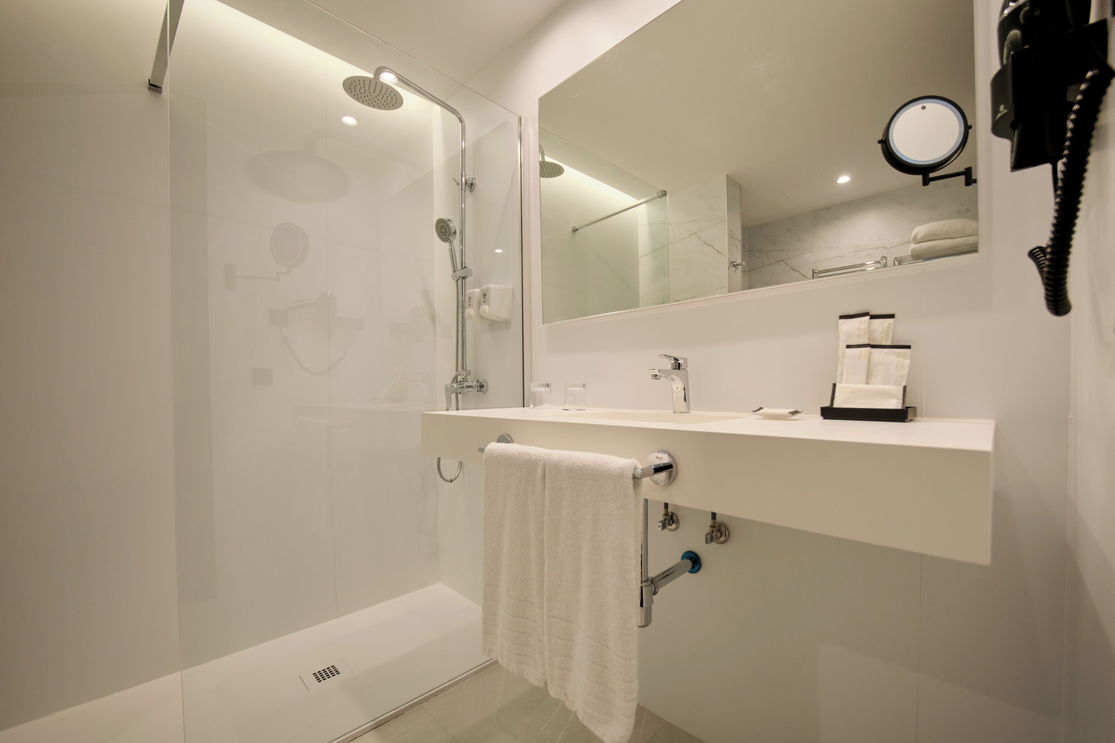 Un baño moderno con ducha de vidrio, un lavamanos blanco con espejo arriba y un toallero con una toalla blanca.