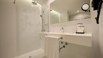 Un baño moderno con ducha de vidrio, un lavamanos blanco con espejo arriba y un toallero con una toalla blanca.
