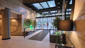 A modern hotel lobby with a glass entrance, large columns, and indoor plants. - 1881 Madrid Ventas Hotel (Madrid)