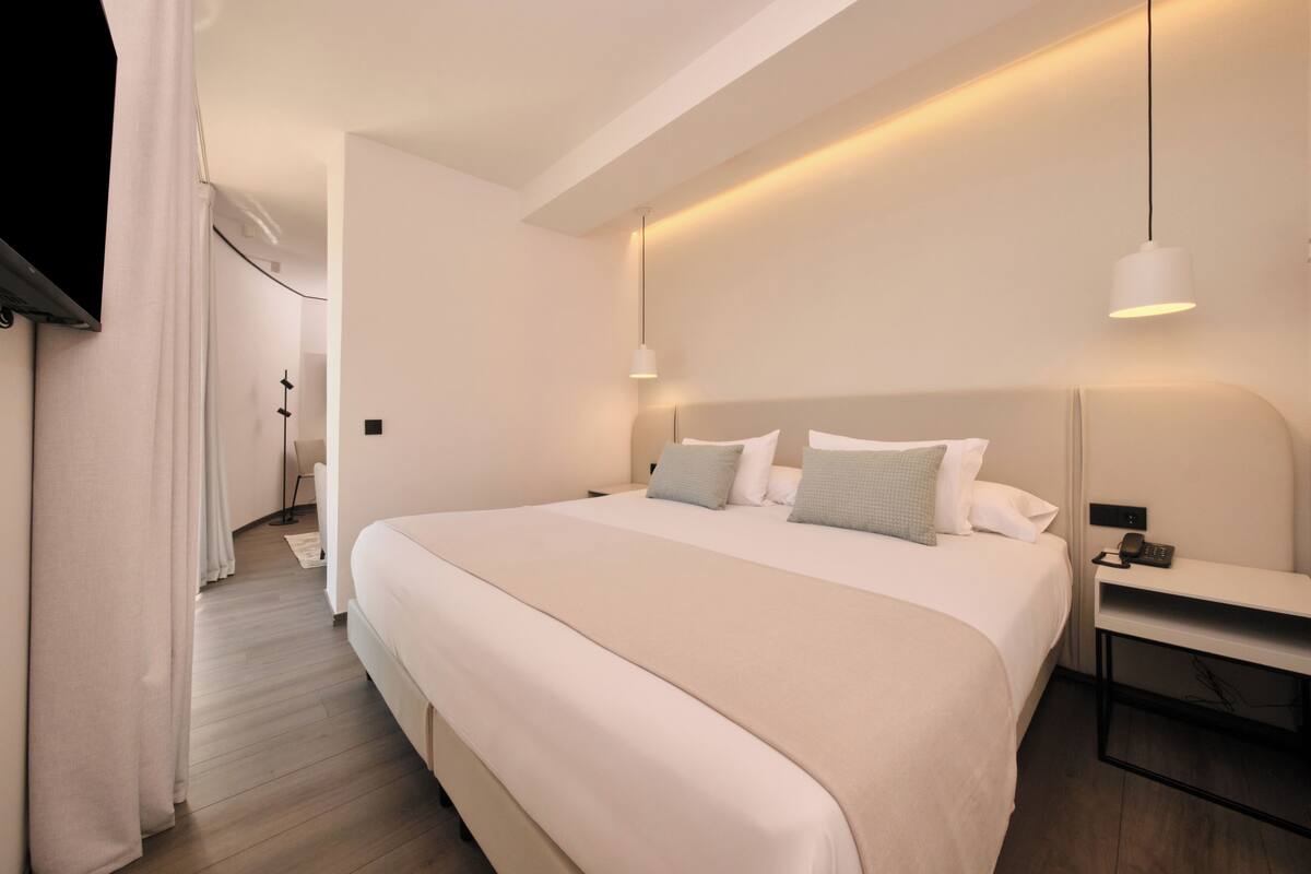 A modern hotel room with a large bed, bedside tables, and a nightstand.