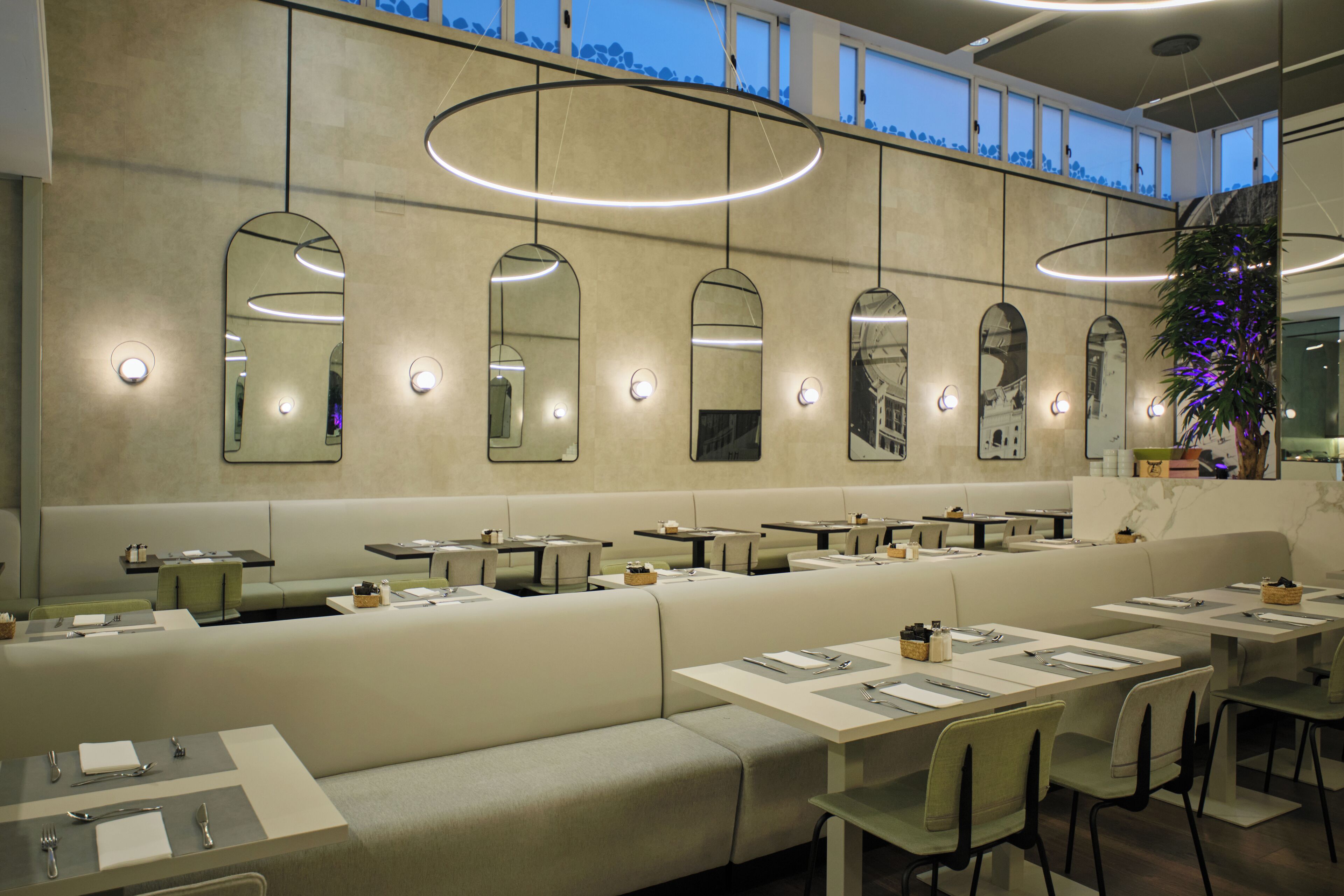 Een modern restaurant met hoge plafonds, inbouwverlichting en een lange balie met zitplaatsen.
