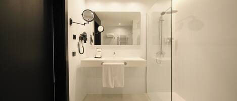 Un baño moderno con cabina de ducha de vidrio, un lavamanos blanco con una toalla y un espejo.