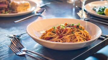 A dining table with a bowl of pasta, cutlery, and a glass of wine.
