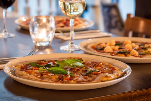 A dining table with plates of pizza and glasses of wine.