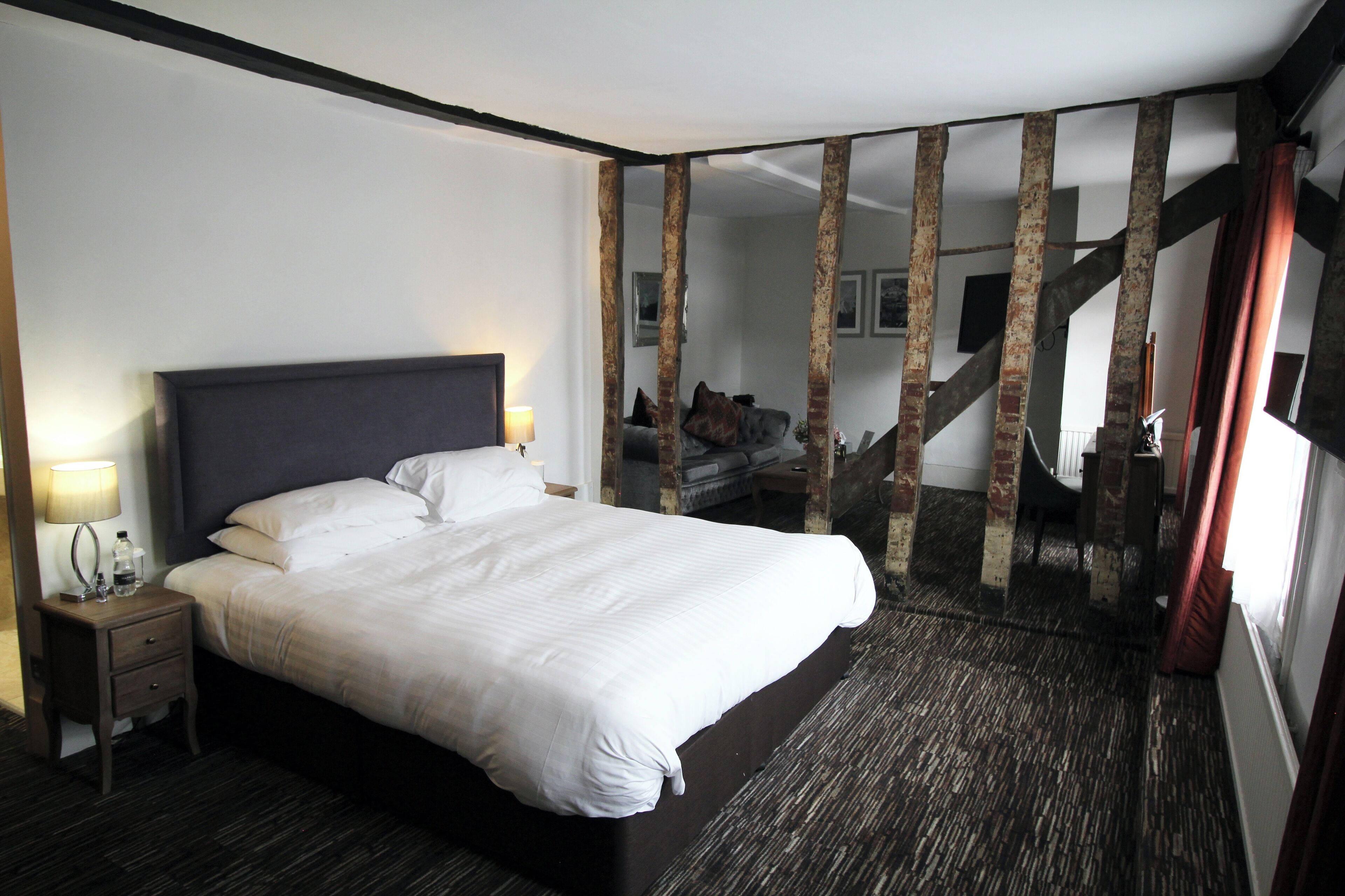 A hotel room with a large bed, a nightstand with a lamp, and a view of a staircase.