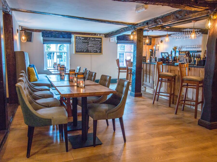 Un restaurante con una larga mesa de madera y varias sillas, una zona de bar con taburetes y un menú en una pizarra en la pared.
