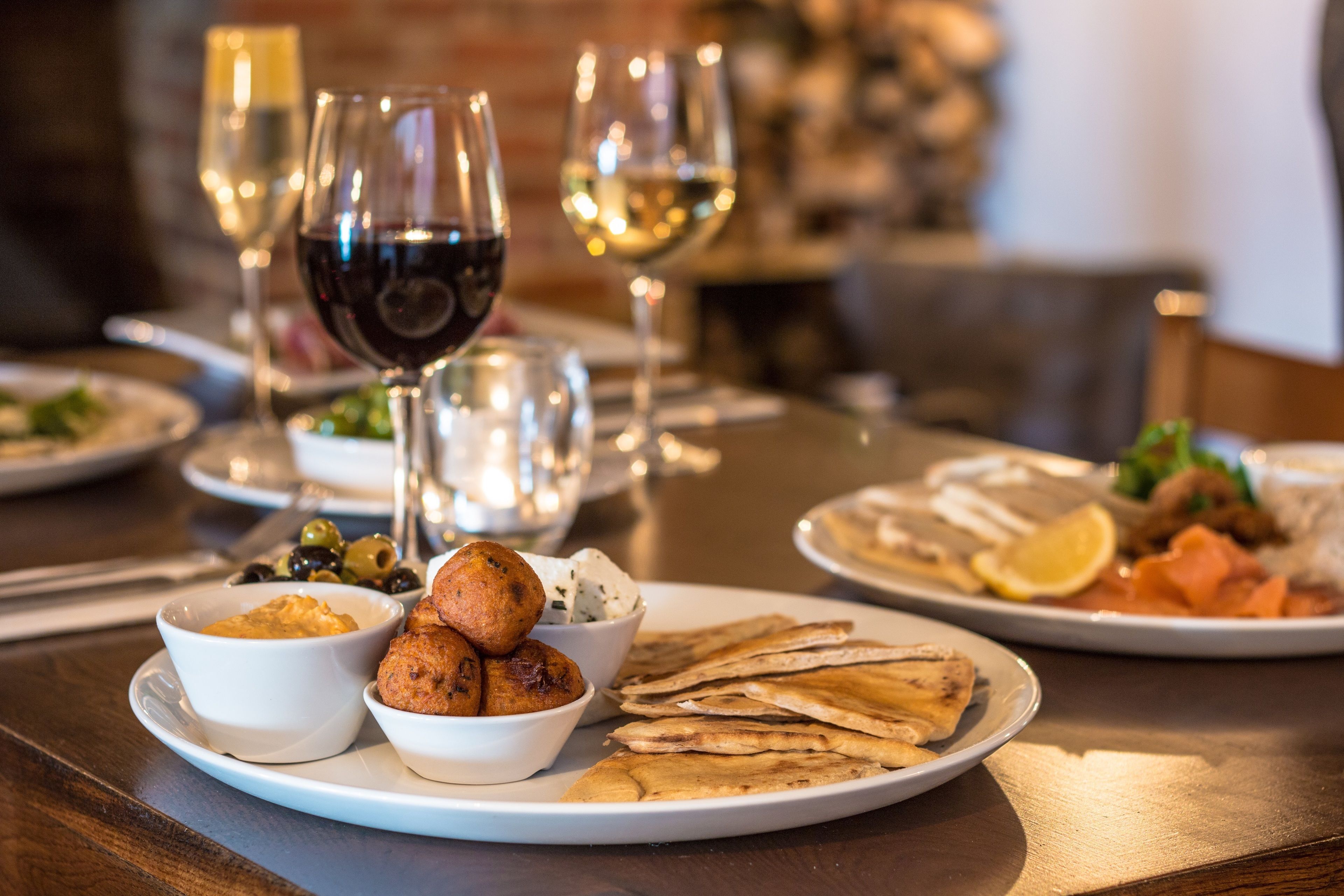 A dining table with various dishes, including flatbreads, olives, and a bowl of hummus.
