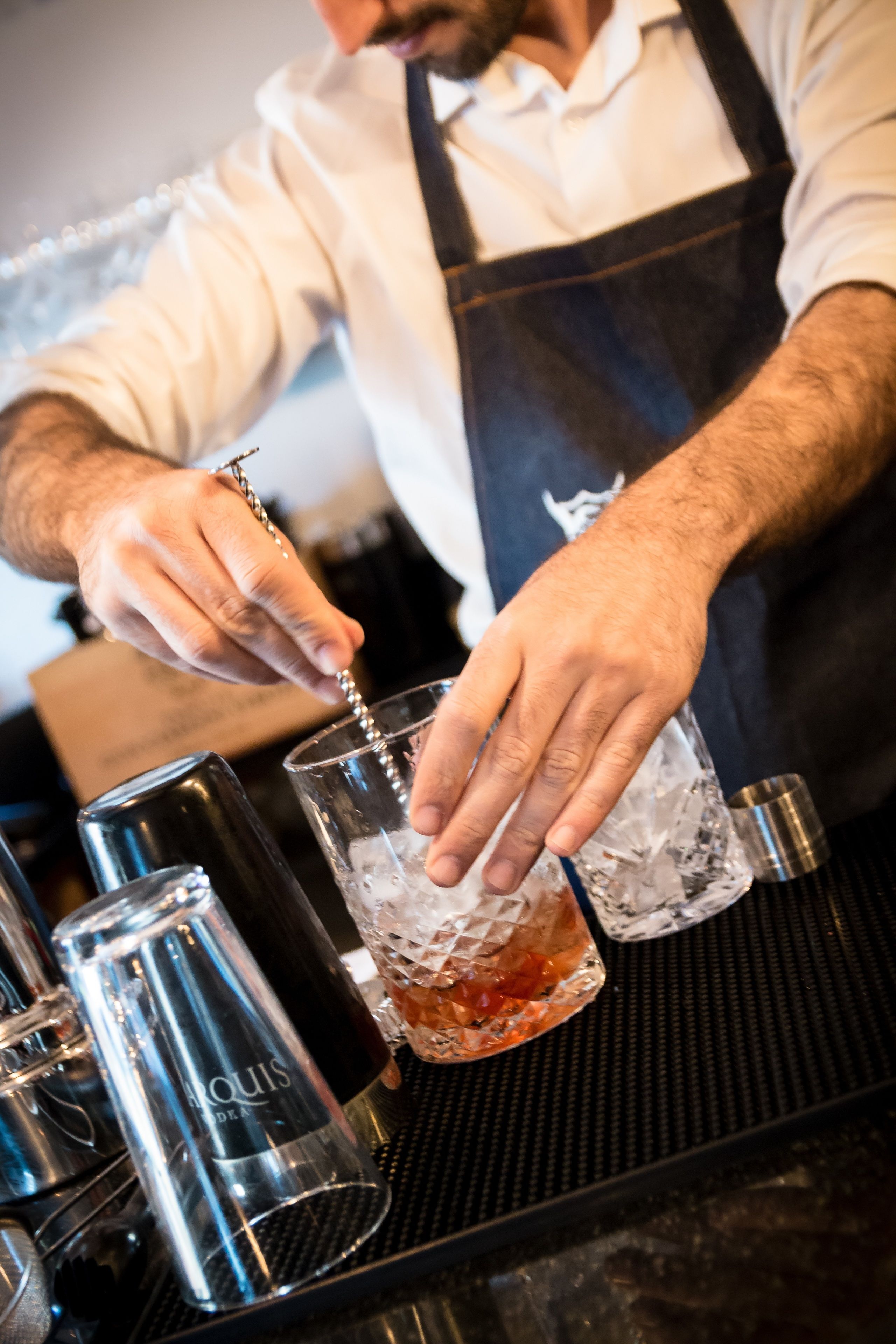 Un cantinero preparando una bebida con un agitador y una copa sobre la barra.