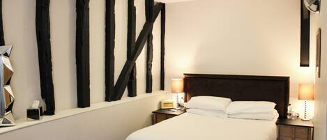 Habitación de hotel con una cama grande, una mesita de noche con lámpara, una pequeña mesa con radio y una pared con arte abstracto en blanco y negro.