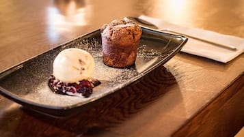 Un postre sobre un plato negro con un muffin y una bola de helado.