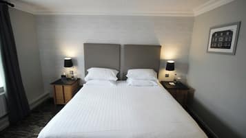 Una cama bien hecha con sábanas blancas, dos mesitas de noche con lámparas y un cuadro en la pared.