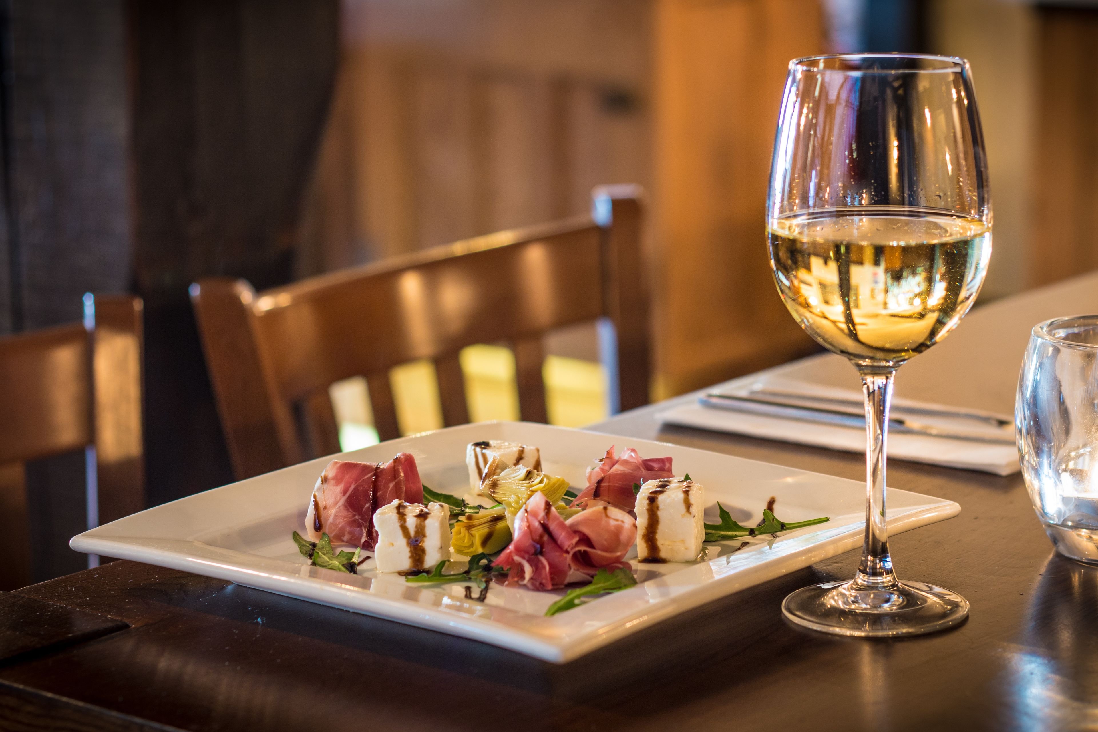 Une table à manger avec une assiette blanche remplie de nourriture, un verre à vin et une chaise en bois.