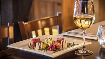 Une table à manger avec une assiette blanche remplie de nourriture, un verre à vin et une chaise en bois.