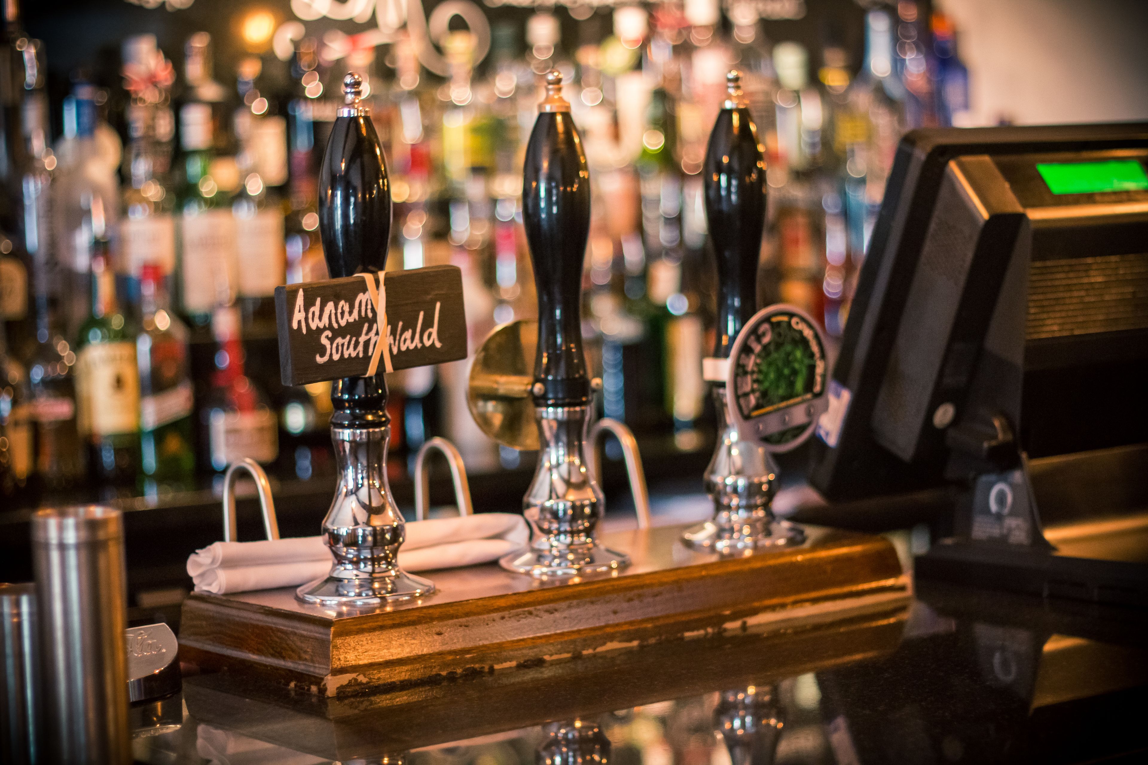 A bar counter with tap handles labeled "Adams Southland" and a digital payment terminal.